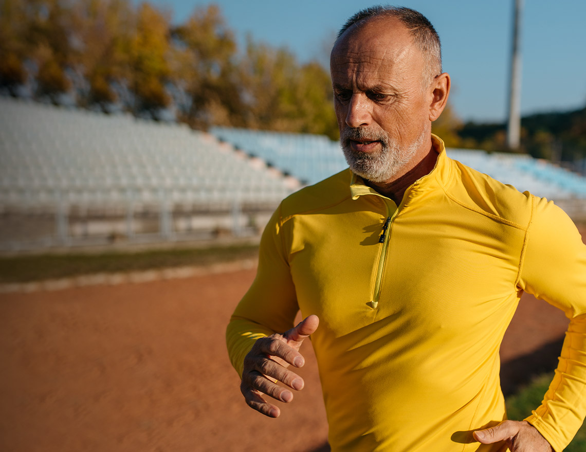 Man with gray hair and yellow shirt running on a track